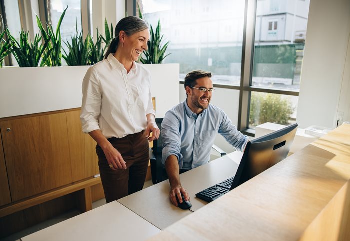 two employees smiling and looking at computer in office