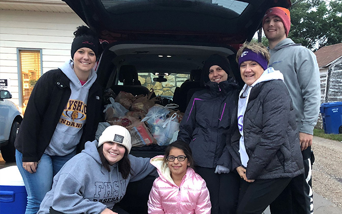 group of people by open car trunk with donations