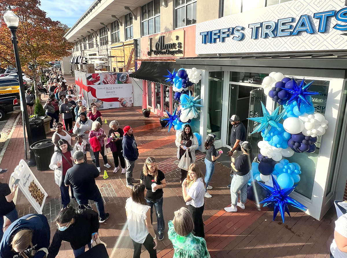 a lot of people standing outside a grand opening with balloons
