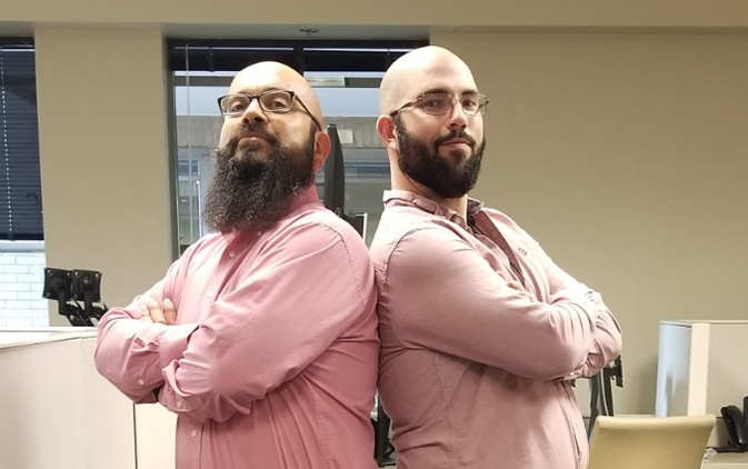 two men standing back to back with arms crossed in matching pink shirts
